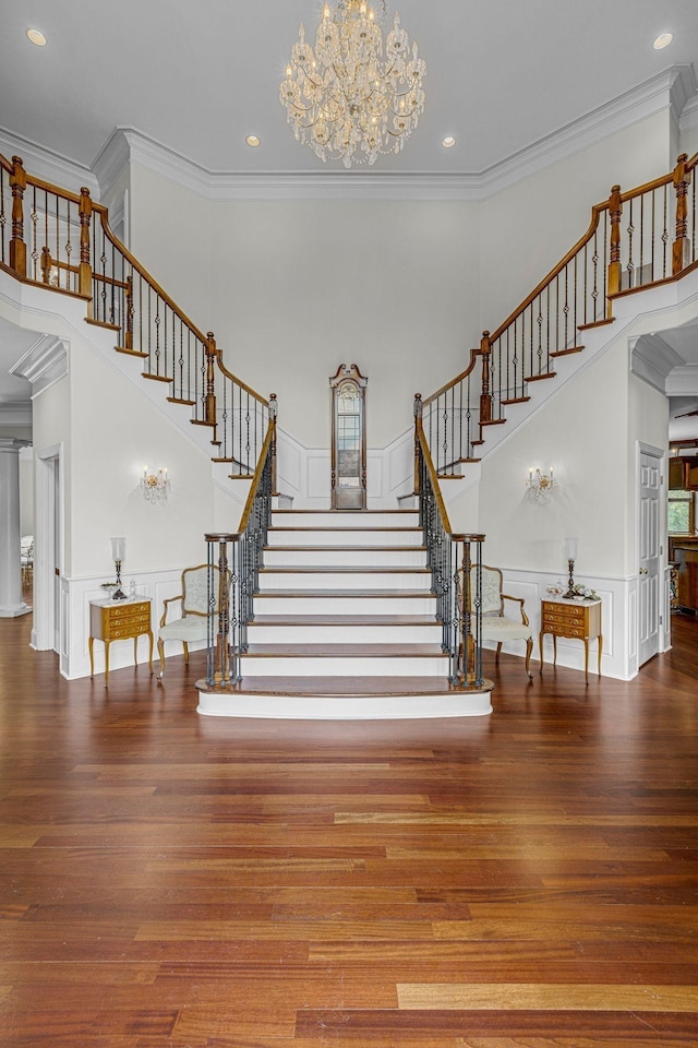 staircase featuring a notable chandelier, ornamental molding, wood finished floors, a high ceiling, and a decorative wall