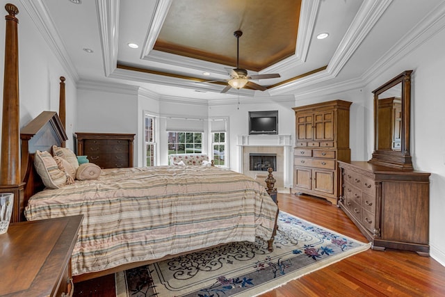 bedroom with light wood finished floors, a tray ceiling, recessed lighting, a fireplace, and crown molding