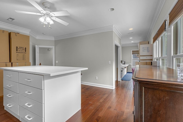 kitchen with baseboards, a kitchen island, ceiling fan, ornamental molding, and dark wood-type flooring