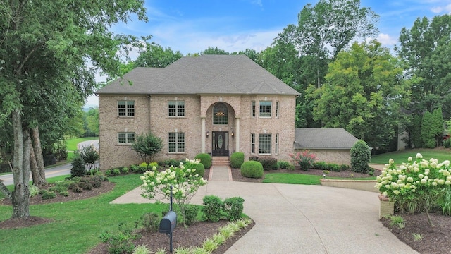 view of front of home with a front yard, brick siding, driveway, and roof with shingles