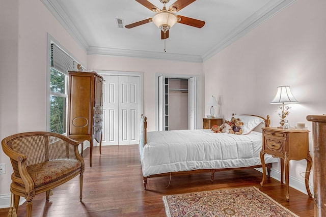 bedroom featuring a ceiling fan, baseboards, wood finished floors, ornamental molding, and multiple closets