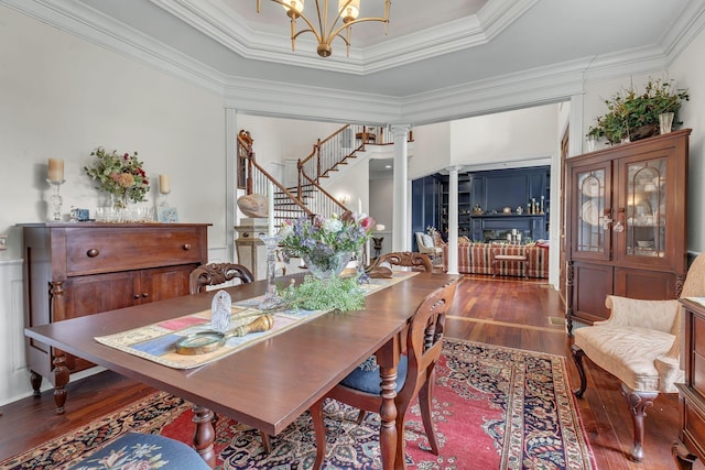 dining room with a notable chandelier, ornamental molding, wood finished floors, stairway, and decorative columns