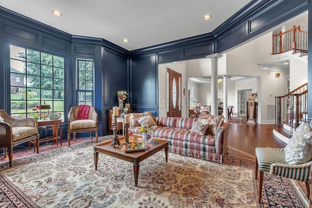 living area with stairway, ornamental molding, wood finished floors, a decorative wall, and ornate columns