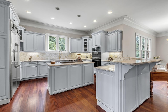 kitchen with a kitchen island, glass insert cabinets, light stone countertops, a peninsula, and dark wood-style floors