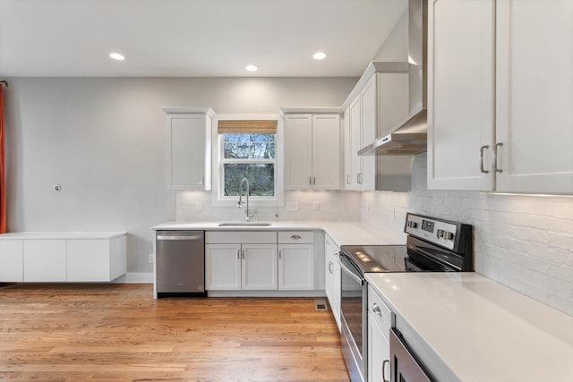 kitchen featuring light countertops, appliances with stainless steel finishes, light wood-style floors, wall chimney exhaust hood, and a sink