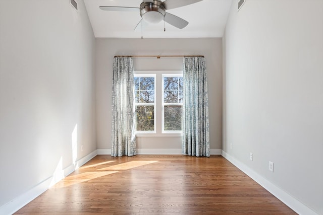 unfurnished room with a ceiling fan, wood finished floors, visible vents, and baseboards