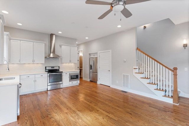 kitchen with visible vents, light wood finished floors, light countertops, appliances with stainless steel finishes, and wall chimney exhaust hood