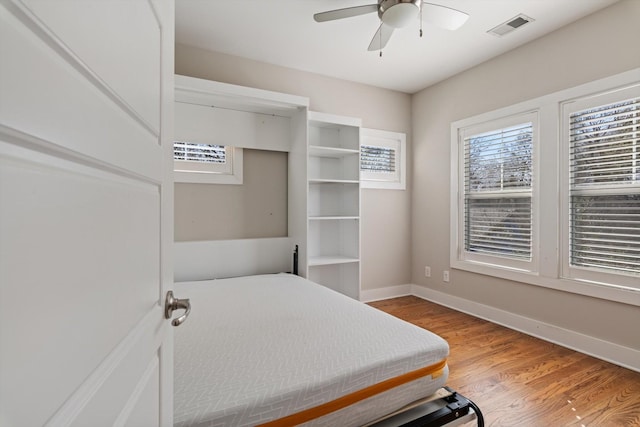 bedroom with ceiling fan, visible vents, baseboards, and wood finished floors