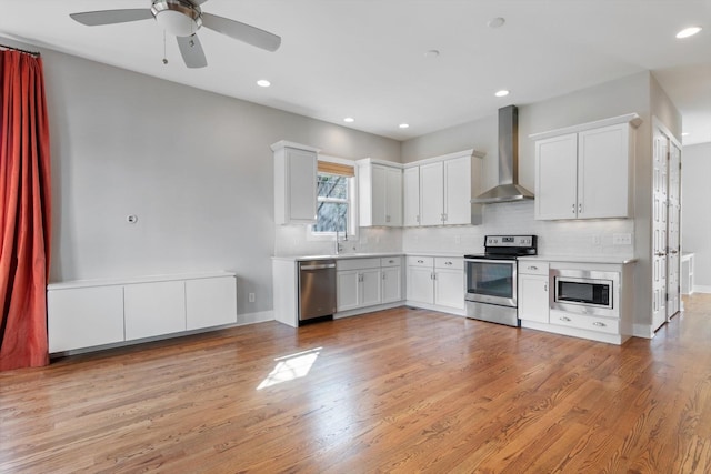 kitchen with light wood-style floors, backsplash, appliances with stainless steel finishes, and wall chimney exhaust hood