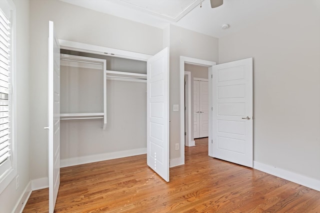 unfurnished bedroom featuring ceiling fan, baseboards, attic access, light wood-type flooring, and a closet