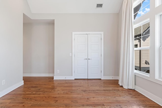 unfurnished bedroom featuring visible vents, baseboards, a closet, and wood finished floors