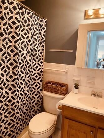 full bath with tile walls, toilet, a shower with shower curtain, wainscoting, and vanity