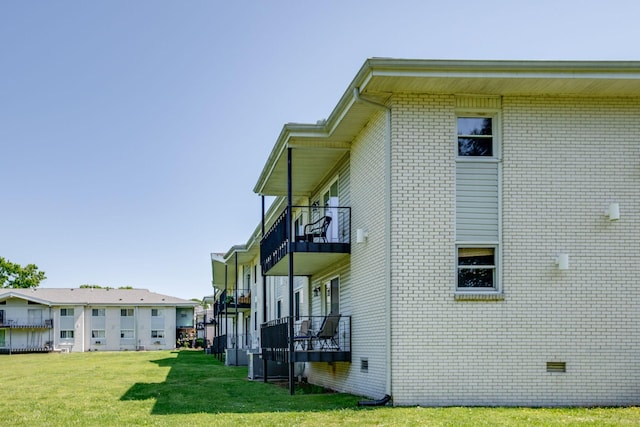 view of side of home featuring a lawn, brick siding, crawl space, and a balcony