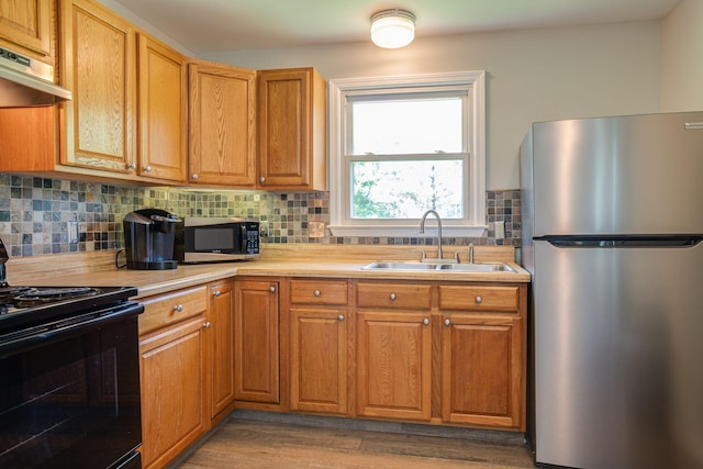 kitchen with decorative backsplash, light countertops, under cabinet range hood, a sink, and stainless steel appliances