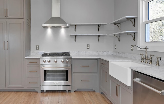 kitchen featuring open shelves, gray cabinets, a sink, appliances with stainless steel finishes, and wall chimney exhaust hood