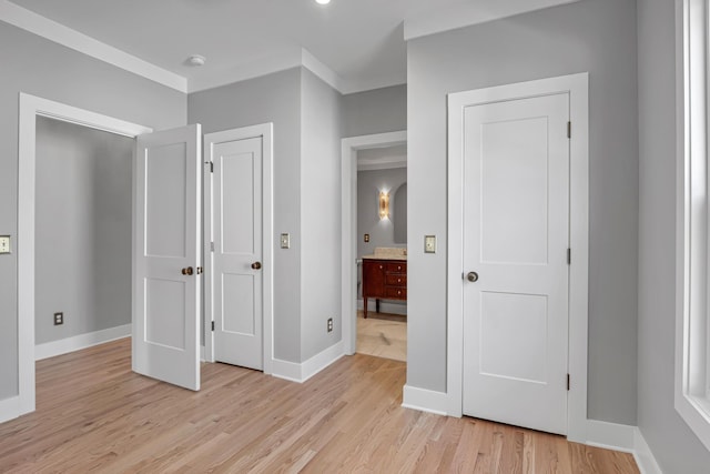 unfurnished bedroom featuring connected bathroom, light wood-style floors, baseboards, and ornamental molding