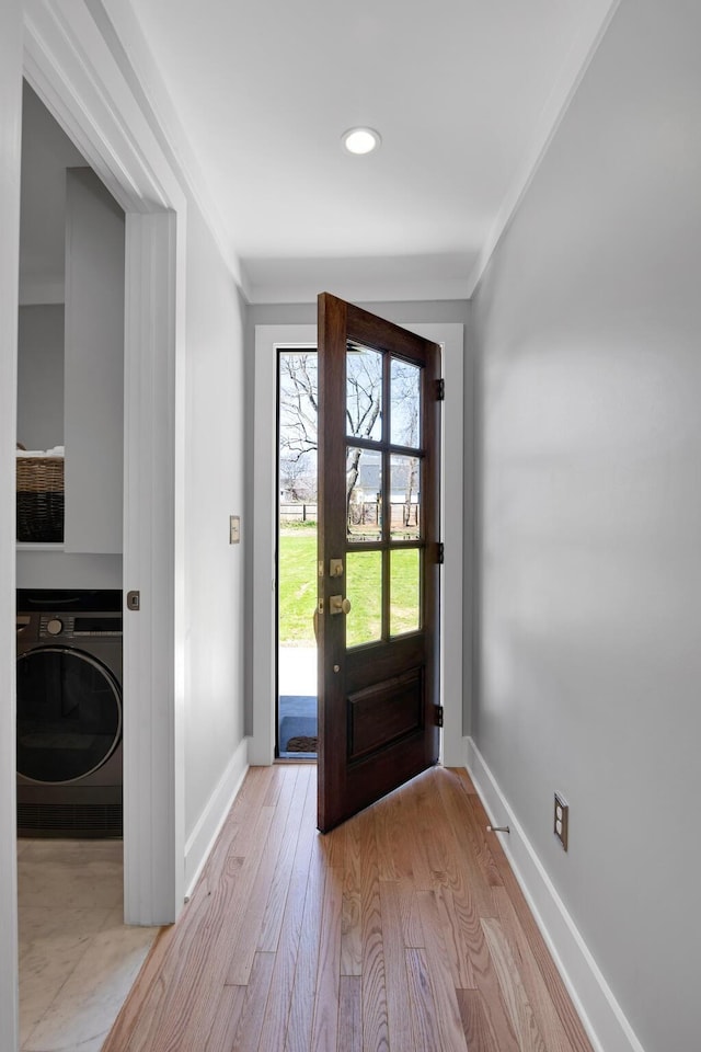 foyer featuring washer / dryer, baseboards, light wood-style floors, and ornamental molding