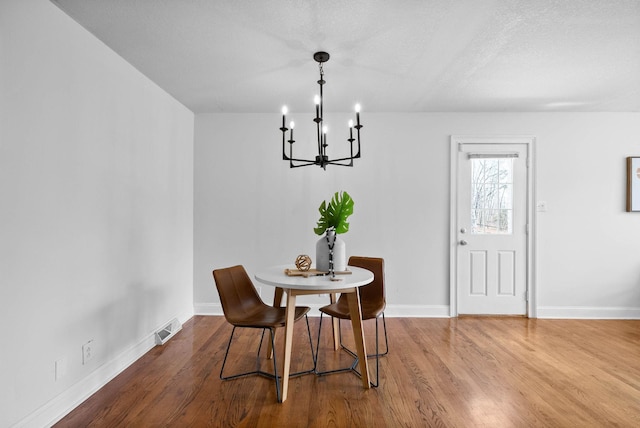 dining space with visible vents, a textured ceiling, wood finished floors, an inviting chandelier, and baseboards