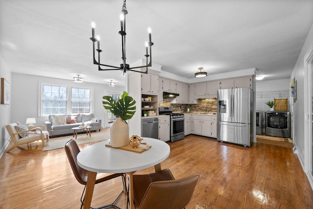 dining room with washing machine and clothes dryer, a chandelier, and light wood-style floors