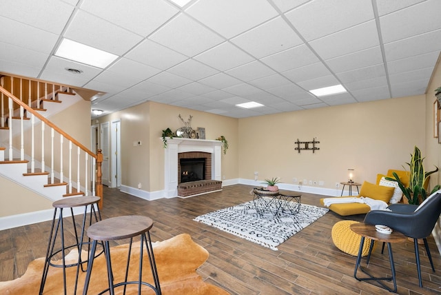 living area with a drop ceiling, stairs, baseboards, and wood finished floors