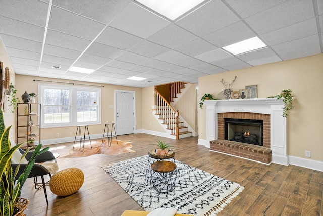 living area with stairway, a drop ceiling, and wood finished floors