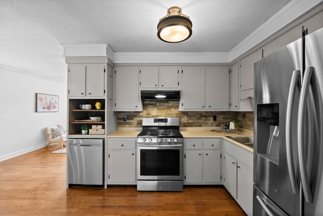 kitchen featuring backsplash, under cabinet range hood, light countertops, appliances with stainless steel finishes, and dark wood-style floors