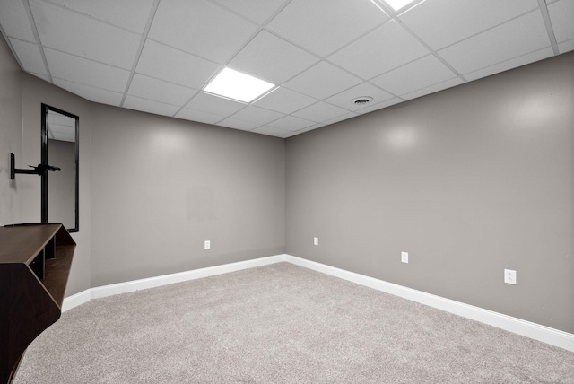 basement featuring a drop ceiling, baseboards, and carpet