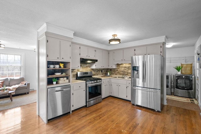 kitchen featuring separate washer and dryer, a sink, light countertops, under cabinet range hood, and appliances with stainless steel finishes