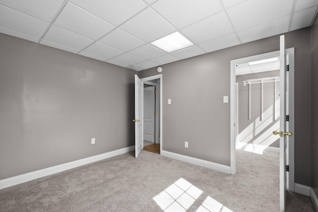 unfurnished bedroom featuring a spacious closet, a drop ceiling, baseboards, and carpet floors