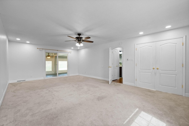 carpeted empty room featuring visible vents, baseboards, recessed lighting, arched walkways, and a ceiling fan