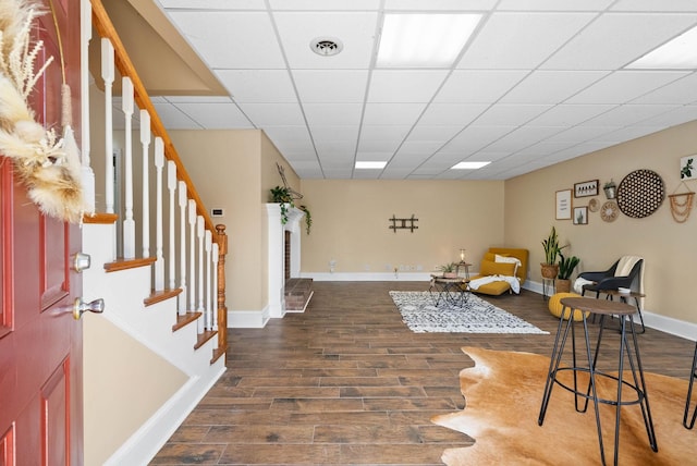 living area with stairs, wood finished floors, visible vents, and a drop ceiling