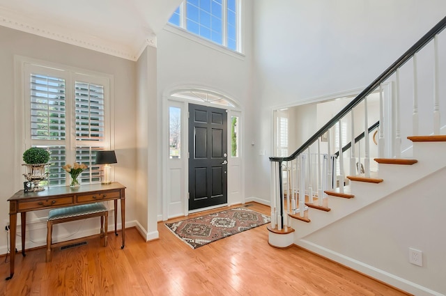 entryway featuring visible vents, wood finished floors, baseboards, a towering ceiling, and stairs