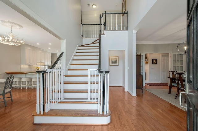 staircase with a notable chandelier, wood finished floors, baseboards, and a towering ceiling