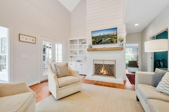 living area featuring baseboards, light wood finished floors, high vaulted ceiling, recessed lighting, and a brick fireplace