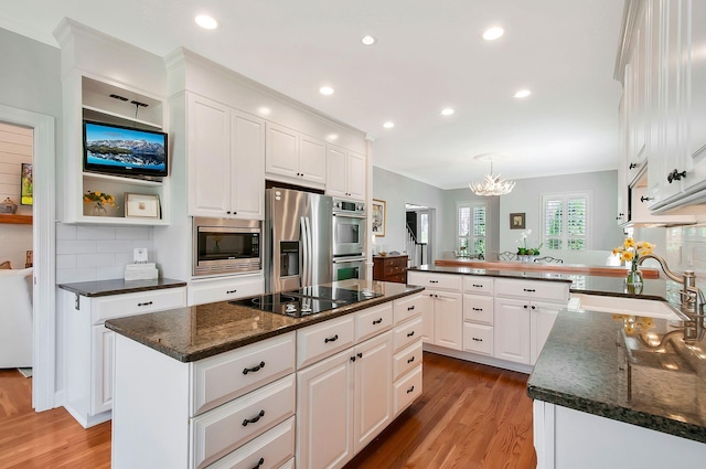 kitchen featuring light wood finished floors, a peninsula, stainless steel appliances, an inviting chandelier, and white cabinetry