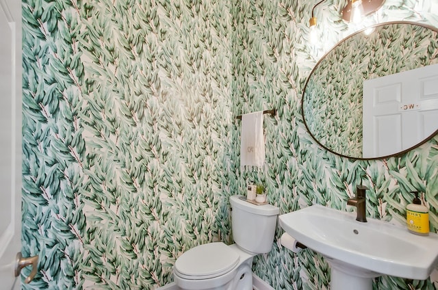 bathroom with toilet, wallpapered walls, and a sink