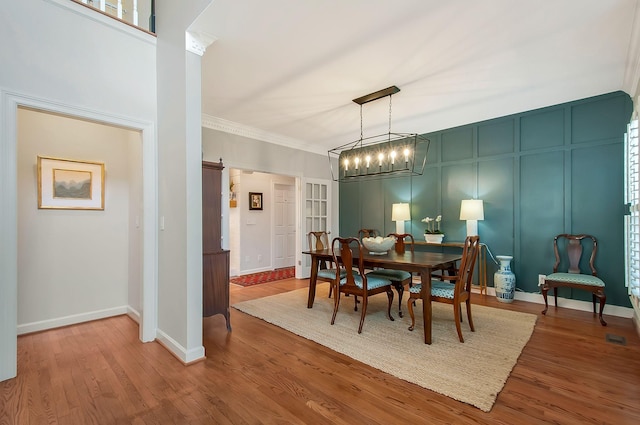 dining room with baseboards, wood finished floors, ornamental molding, and a decorative wall