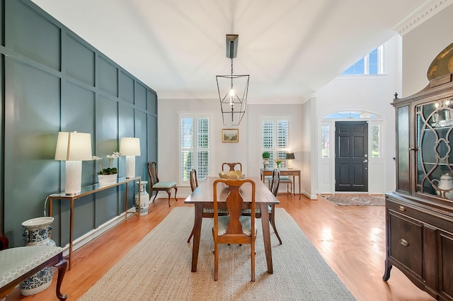 dining room featuring light wood-type flooring, crown molding, and a decorative wall