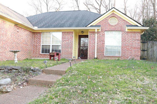 ranch-style house featuring brick siding, roof with shingles, a front yard, and fence