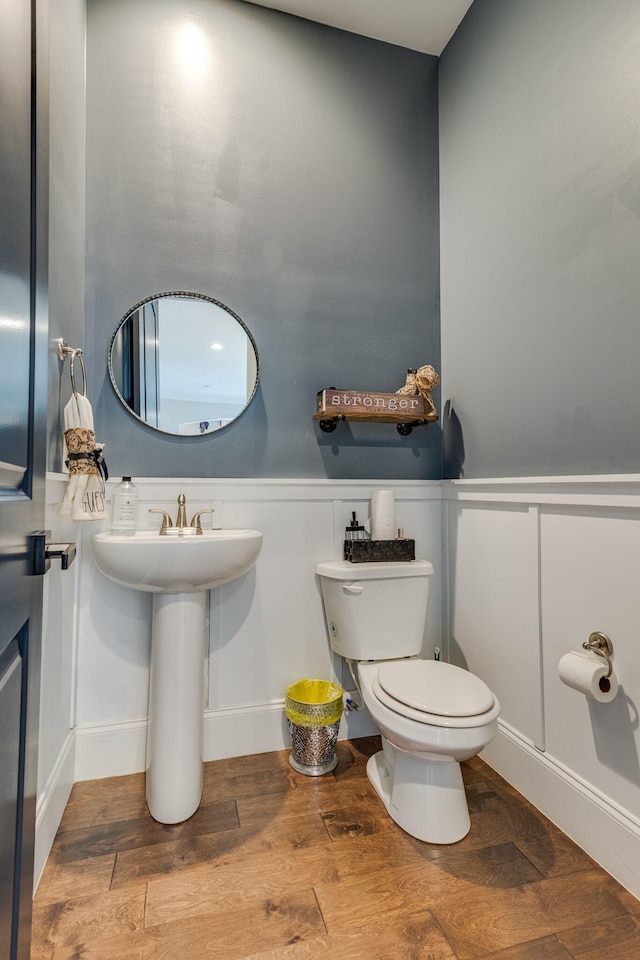 half bathroom featuring a wainscoted wall, toilet, and wood finished floors