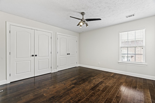 unfurnished bedroom with visible vents, baseboards, a textured ceiling, and dark wood-style floors