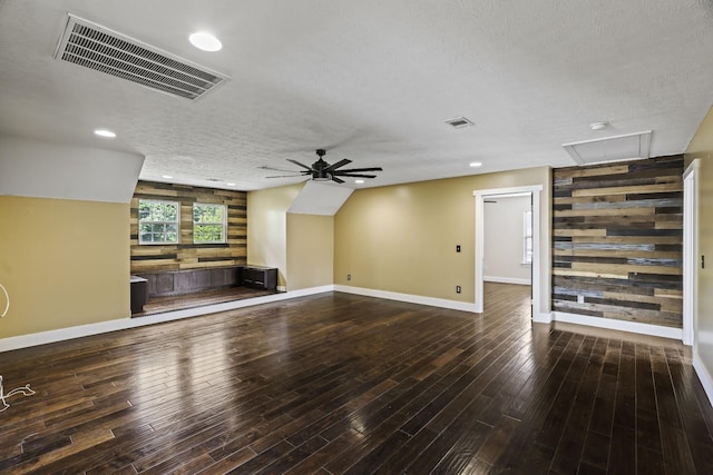 unfurnished living room with visible vents, wood walls, ceiling fan, and wood finished floors