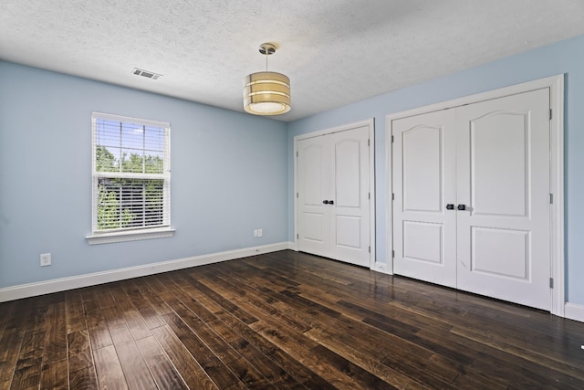 unfurnished bedroom with baseboards, visible vents, dark wood finished floors, a textured ceiling, and two closets