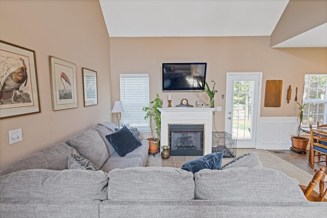 living room with vaulted ceiling, a decorative wall, a fireplace, and a wainscoted wall