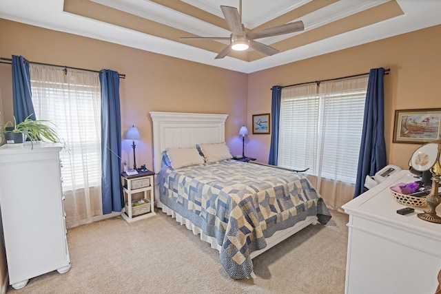 bedroom featuring a raised ceiling, light colored carpet, and a ceiling fan