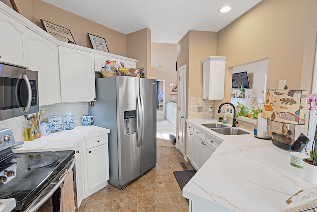 kitchen featuring light stone counters, decorative backsplash, appliances with stainless steel finishes, white cabinetry, and a sink