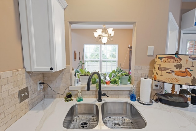 kitchen featuring white cabinets, light stone counters, a chandelier, and a sink