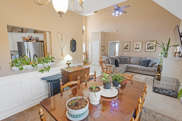 dining space with a decorative wall, high vaulted ceiling, ceiling fan, and a wainscoted wall