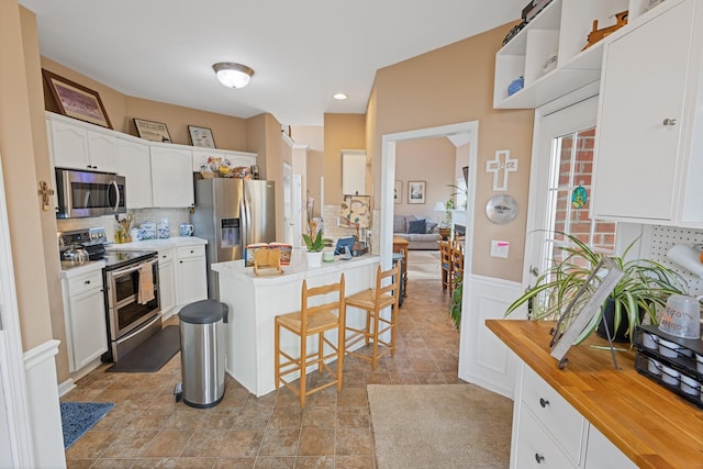 kitchen with appliances with stainless steel finishes, a breakfast bar, wainscoting, and white cabinets