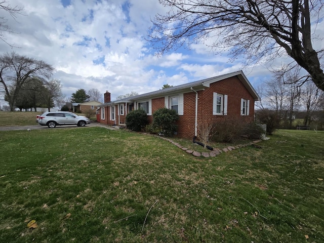 view of side of property with a lawn, brick siding, and a chimney